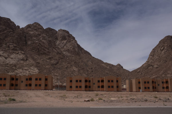 Concrete apartment buildings stand empty across between mountains in St. Catherine, South Sinai, Egypt; a protected mountainous area inhabited by native Bedouin communities. In disregard to environmental laws and Bedouin culture the blocks were built by the government as housing services for the Bedouin locals and workers coming from across the country. Nevertheless, nature and tradition remain to dominate space. These buildings represent the long standing power struggle and tension between the government and the local Bedouin community. Connected to the land by blood, the Bedouin community’s knowledge of the mountains and movements within it intimidates a government that seeks control and sole power. April 2019.